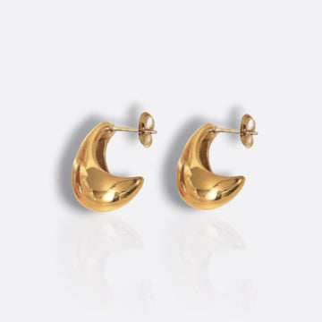 two gold earrings with shadows on a white background. felicia teardrop earring from dinot curated. 18k gold plated, slightyl teardrop shaped earrning with a post friction post earring back. white background with shadows.  